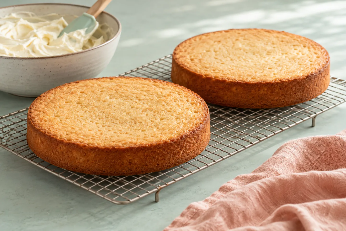 Two unfrosted cake layers cooling separately on a wire rack
